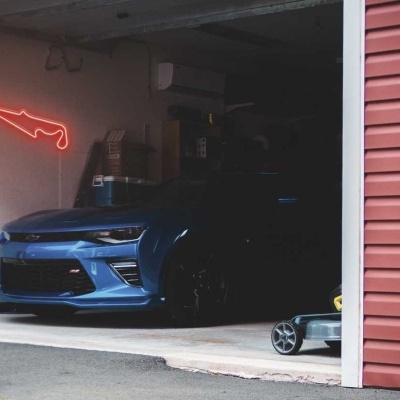 Carro desportivo azul numa garagem com parede branca e néon vermelho