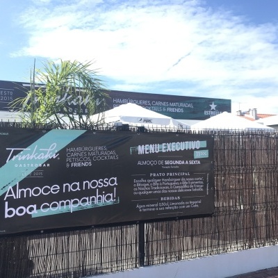 Painel publicitário externo de restaurante com menu executivo, cerca de junco e céu azul