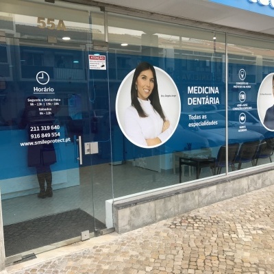 Entrada de clínica dentária com vidro e informações em azul e branco