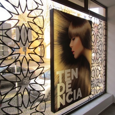 Painel publicitário com fotografia de mulher e texto TENDENCIA na montra com vitral floral