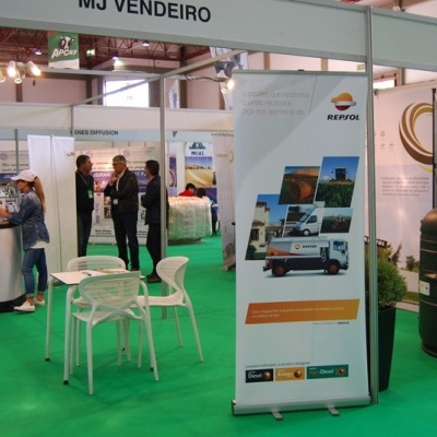 Stand MJ VENDEIRO em feira com mesa, cadeiras, banner REPSOL e tanque preto cilíndrico.