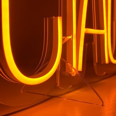 Letreiro luminoso em néon laranja com letras montado numa base transparente