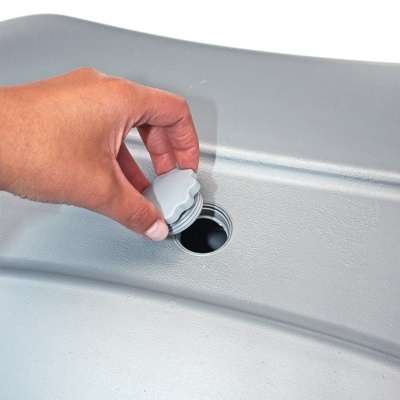 Mão a segurar tampa cinzenta de plástico junto a abertura circular numa superfície cinzenta.