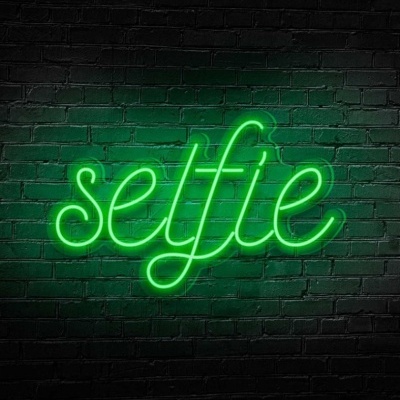 Sinal de néon verde com a palavra 'selfie' numa parede preta de tijolos