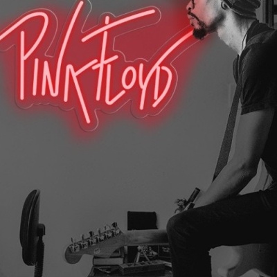 Homem sentado com guitarra elétrica e letreiro rosa Pink Floyd