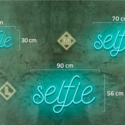 Letreiros de neon azuis com a palavra 'selfie' em vários tamanhos numa parede cinza.