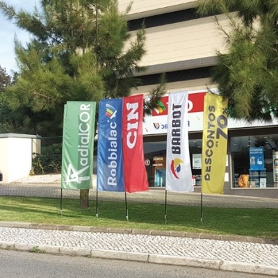 Cinco bandeiras verticais coloridas com texto e edifício ao fundo