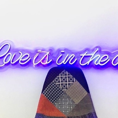 Letreiro neon roxo com a frase Love is in the air na parede