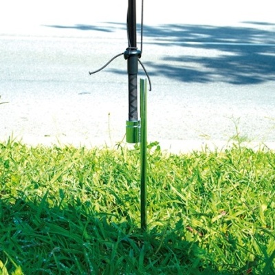 Estaca de metal preta com suporte e dispositivo verde no chão de relva junto a estrada