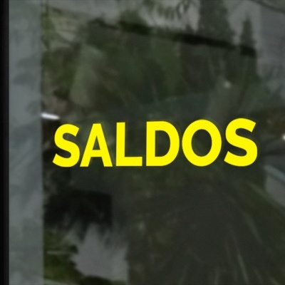 Texto em letras amarelas 'SALDOS' numa porta ou janela de vidro