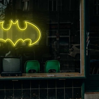 Letreiro neon amarelo em montra com símbolo do Batman e cadeiras verdes