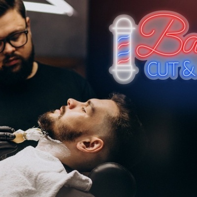 Barbeiro atende cliente com toalha branca e sinal de néon Barber CUT & SHAVE
