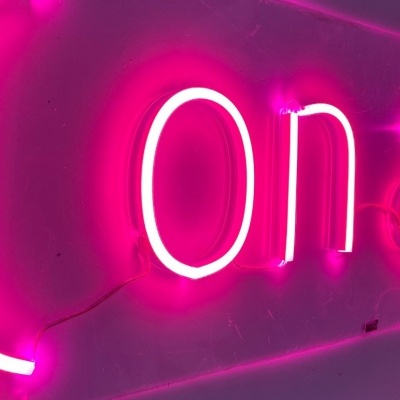 Placa neon rosa 'On air' com luz brilhante numa parede branca