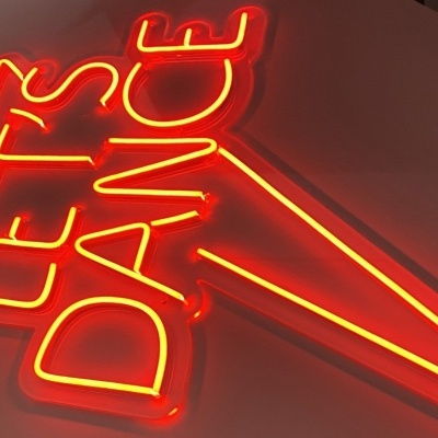Sinal luminoso neon vermelho com texto LET'S DANCE numa parede branca
