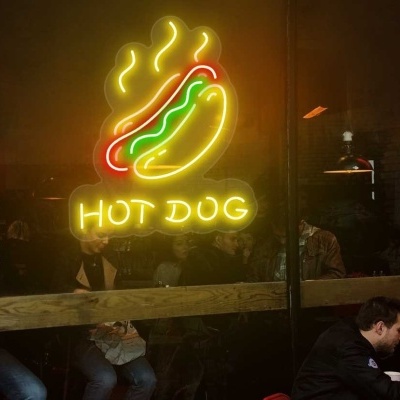 Sinal de néon colorido com cachoro quente e texto HOT DOG numa janela de vidro de um espaço interior