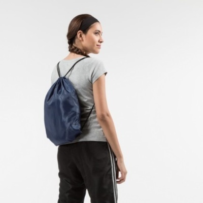 Mochila saco azul escuro com cordões pretos usada por mulher de costas