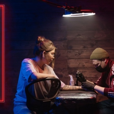 Jovem a fazer tatuagem numa sala escura com sinal de neon TATTOO