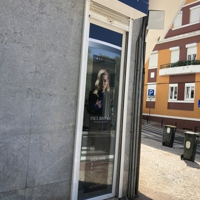 Entrada de loja com placa 'BEAUTY' e anúncio com mulher loira na porta de vidro