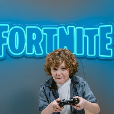 Criança a jogar videojogo com comando preto, fundo cinza com texto FORTNITE em néon azul