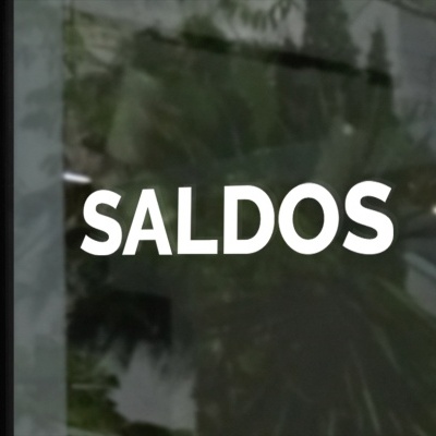 Palavra SALDOS em branco numa superfície de vidro refletindo uma planta e escada atrás