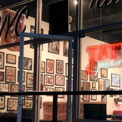 Montra noturna de loja de tatuagens com letreiro neon e quadros de desenhos