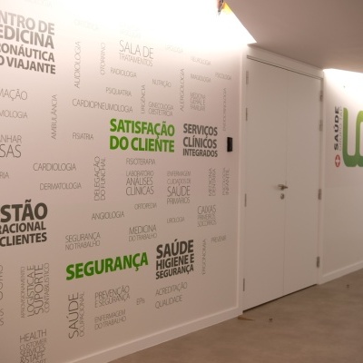 Corredor com parede branca decorada com palavras em português relacionadas à medicina e serviços clínicos, logotipo LGS ao fundo