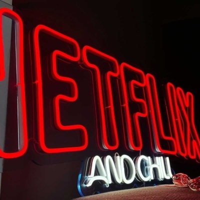 Letreiro neon com a palavra NETFLIX em vermelho e texto AND GHI em branco azul num fundo escuro