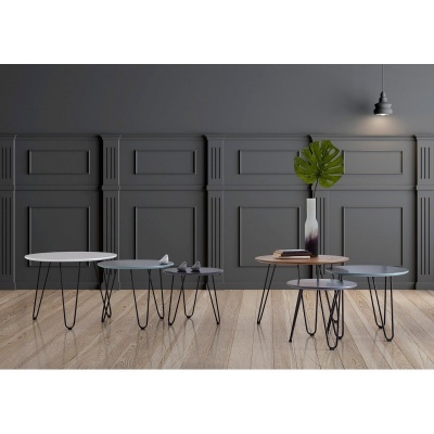 Quatro mesas de centro redondas em diferentes cores com pernas finas pretas, piso de madeira clara e parede cinzenta ao fundo