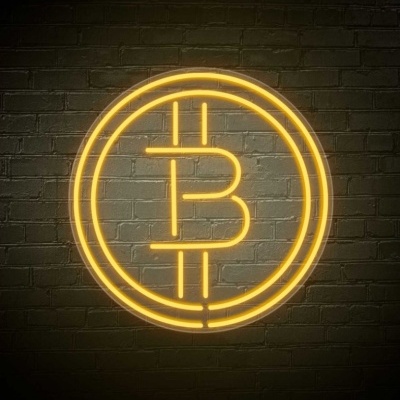 Logótipo do Bitcoin em néon amarelo contra parede de tijolos cinza escuro