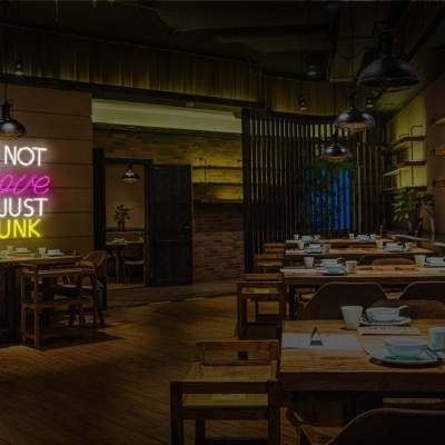 Interior de restaurante com mesas de madeira e placa de néon colorida na parede