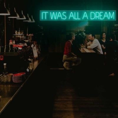 Interior de café com placa luminosa de néon verde com texto 'IT WAS ALL A DREAM'