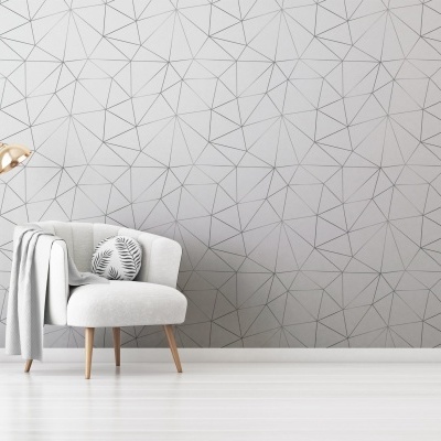 cadeira estofada cinza claro com almofada e candeeiro dourado numa sala com parede cinza geométrica