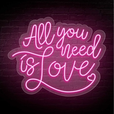 Painel de neon rosa com a frase 'All you need is Love' numa parede de tijolos escuros