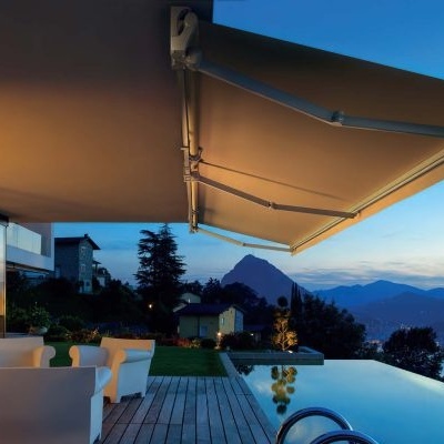 Toldos retráteis bege sobre varanda com poltronas brancas e piscina de borda infinita ao entardecer