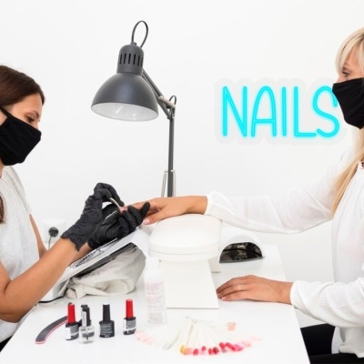 Manicure profissional com duas mulheres usando máscaras pretas num salão de unhas