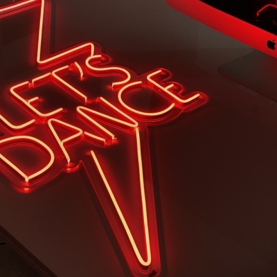 Placa de néon vermelha LET'S DANCE em forma de raio numa secretária com computador