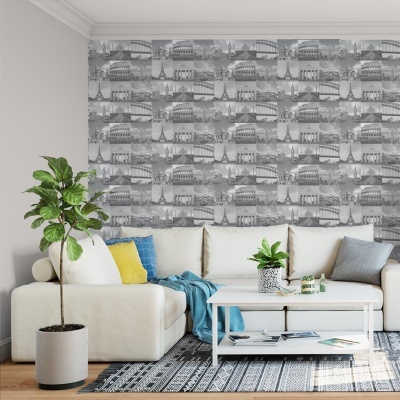 Sala de estar com sofá branco em canto, almofadas coloridas, mesa branca, plantas e papel de parede cinza com ilustrações de pontos turísticos.