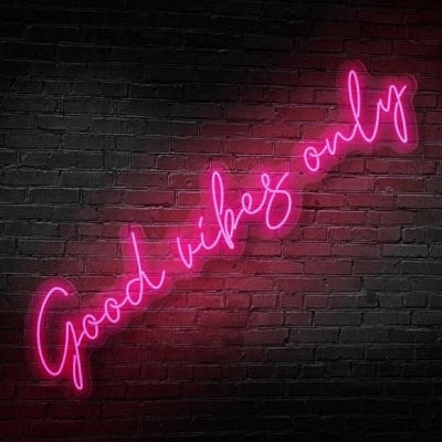 Letreiro néon cor-de-rosa com texto Good vibes only numa parede de tijolos pretos