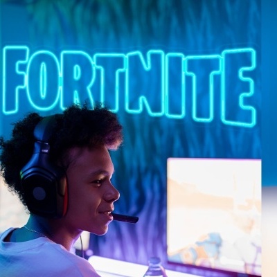 Jogador com auscultadores frente a ecrã de computador com iluminação azul e texto FORTNITE no fundo