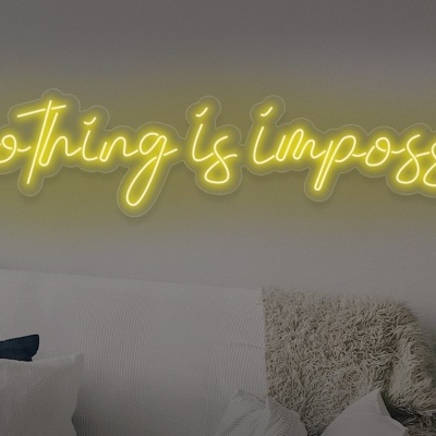Placa de néon amarela com a frase 'nothing is impossible' acima de um sofá branco com mantas e almofadas.