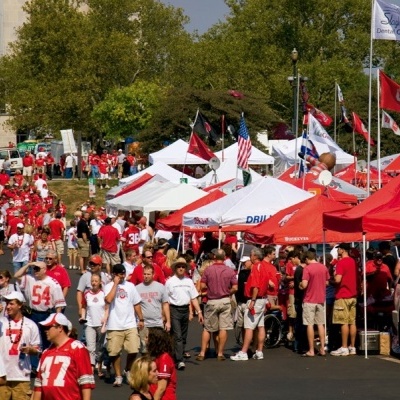 Evento ao ar livre com tendas, bandeiras e pessoas em camisolas desportivas vermelhas e brancas