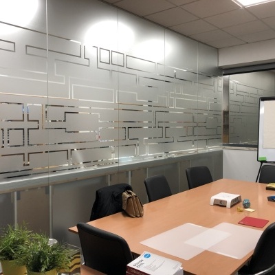 Sala de reuniões com mesa de madeira, cadeiras pretas, projetor, planta e parede de vidro decorada