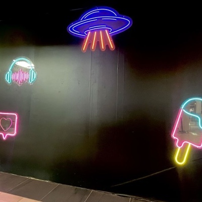 Luzes de néon coloridas numa parede preta com diversas figuras e texto