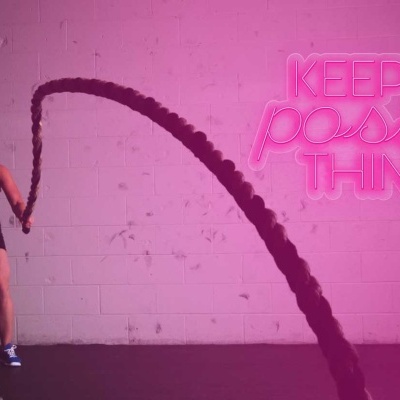 Mulher a fazer exercício com corda de batalha negra perto de parede com texto em néon rosa