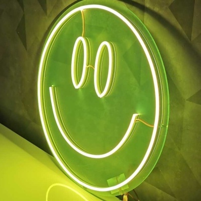 Letreiro de néon em forma de rosto sorridente amarelo sobre superfície verde