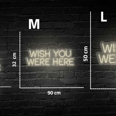 Três letreiros luminosos com texto 'WISH YOU WERE HERE' em três tamanhos diferentes numa parede de tijolos pretos.