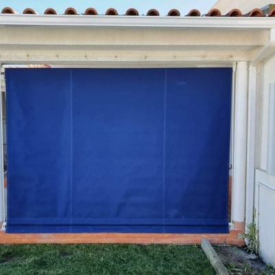 Toldo azul escuro esticado entre colunas brancas numa varanda com telhado de telhas vermelhas