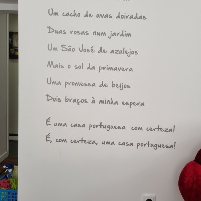 Parede branca com texto em português, tomada e parte de sofá vermelho