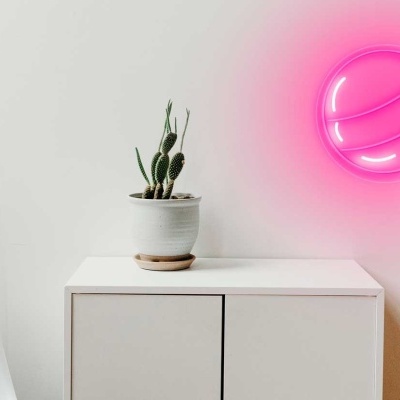 cadeira branca, mesa branca com planta em vaso e luz de néon em forma de pirulito