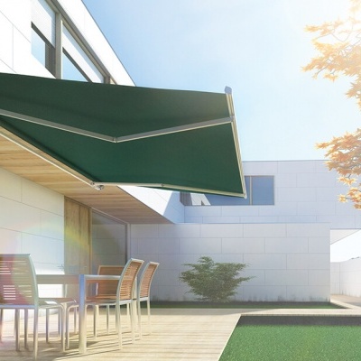 Toldo verde escuro retrátil acima de mesa com quatro cadeiras em terraço com chão de madeira e relvado artificial